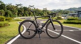 Sleek black road bike parked on a curved cycling path, surrounded by lush greenery and open sky.