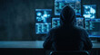 © NikProArt - Anonymous hacker in a hoodie sitting in front of multiple computer monitors in a dark room