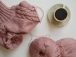 © evghenia - Top view flat lay of unfinished pink knitted sweater on circular needles, skeins of yarn and cup of coffee on white background, cozy knitting hobby and autumn craft concept
