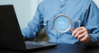 © Krittamet - Auditing, banking compliance, financial investigation, law, risk assessment and verification. Businessman using a laptop and magnifying glass to examine financial documents and legal information.
