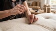 © Bashra - Upholsterer sewing a button on a fabric cushion in a professional furniture workshop