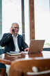© svetlana_cherruty - Mature businessman talks on smartphone while working with laptop at office table, with large copy space for business advertising. Vertical format.