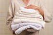 © Marc Tran/Stocksy - Woman holding a neat stack of clean, fluffy white and cream towels