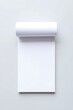 © Majethiya - Blank white paper notepad pad with rolled top resting on neutral grey surface