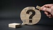 © Shahbaz - Hand placing wooden blocks to complete a speech bubble shape featuring a large black question mark on a dark background