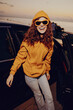 © SHOTPRIME STUDIO - A smiling woman in an orange hoodie stands beside an open car door at sunset, conveying casual fashion, warmth, and carefree energy in a bright, outdoor moment.