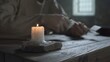 © diablosiatr - Burning candle on a stone base, with the blurred hands of a prisoner cutting a quill pen in the background inside a medieval dungeon cell
