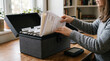 © OKPhics - Woman organizing paper documents into a black file box on a wooden desk