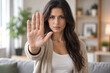 © Miltan - Woman displaying a stopping hand gesture expressing rejection in a domestic setting