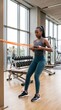 © Rindaman - Dedicated Young African American Woman Performing Strength Training with Resistance Bands in a Modern Sunny Gym Interior for Health and Fitness.