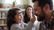 © AIMIN - A silly toddler with a mustache on her forehead tries to put one on dad for Movember fun and family health awareness campaigns.
