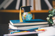 © Manasanan Wongchoomp - Small world globe in a graduation cap rests on stacked books with colorful pencils nearby, representing global education, international learning, study, knowledge, achievement, and student success