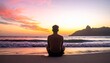 © Dear D - A young man sitting in a meditative pose on a sandy beach observing the calm ocean waves during a vibrant and colorful golden hour sunrise