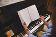 © Taras Grebinets - Woman turning sheet music at a piano keyboard preparing to practice a classical piece