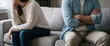© Hasibnikon - A close-up shot of a young couple sitting apart on a gray couch in their living room, experiencing marital conflict, tension, and a communication breakdown in their relationship, reflecting sadness.