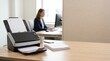 © Sajidh - Scanner sitting on a light wooden desk in an office environment with bright daylight streaming through windows illuminating crisp white paper documents.
