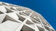 © stock mind's - Low angle view of a modern building facade with a white grid structure and triangular architectural details against a deep blue sky