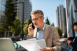 © Davor - Senior businessman on phone with documents outdoors in city