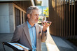 © Davor - Mature businessman using smartphone voice assistant outside office