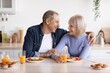© Prostock-studio - Smiling Elderly Caucasian Couple Sitting At Kitchen Table, Enjoying Breakfast With Fresh Foods And Juices, Sharing A Joyful Moment Together In Cozy Home Setting. Happy Relationship Concept.