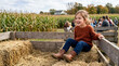 © Xenia - Happy young girl enjoying an autumn hayride on a farm wagon. Child sitting on straw bales near a corn field during fall festival