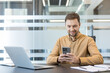 © Liubomir - Digital communication and remote work, professional man using smartphone and laptop for business productivity in modern office. Corporate employee managing tasks with mobile technology and computer.