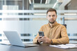 © Liubomir - Digital transformation and remote work, professional man using smartphone at office desk with laptop. Business productivity and corporate communication, modern workplace technology and connectivity.