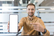 © Liubomir - Mobile app promotion and digital marketing concept, man pointing at blank smartphone screen for mockup in office. Professional business communication and technology strategy.