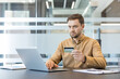 © Liubomir - Online payment and e commerce security, man using credit card for digital shopping on laptop in office. Secure financial transaction and internet banking.
