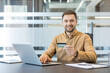 © Liubomir - Online shopping and digital payment, man using credit card and laptop for e commerce transaction in modern office. Secure financial operations and consumer behavior.