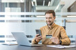 © Liubomir - Online shopping and digital payment, man using smartphone and credit card for e commerce transaction at office desk. Secure financial technology and mobile banking.