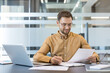 © Liubomir - Productivity and corporate workflow, professional man working at desk with laptop and documents in modern office. Business strategy and data analysis.