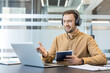 © Liubomir - Remote work and virtual meeting, professional man using laptop and headphones for video conference in modern office. Business communication and digital collaboration, employee participating in online.