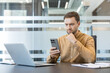 © Liubomir - Work stress and digital burnout, man looking at smartphone with concern in modern office. Professional businessman checking mobile device for urgent business communication and corporate data.