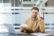 © Liubomir - Work stress and financial anxiety, man reading bad news in a letter at office desk with laptop. Professional employee experiencing burnout and job insecurity while reviewing important documents.