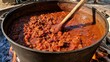 © PinkiePie - Huge pot of chili cooking for a crowd over a large fire pit, stirring with a long wooden spoon