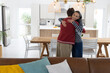 © Wavebreak Media - Couple hugging, female smiling in striped top, male wearing red jacket at wooden dining table