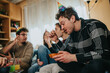 © qunica.com - A group of young friends sit together in a living room wearing party hats and eating snacks. The relaxed home birthday party shows conversation, laughter and casual celebration among peers.