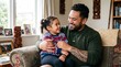 © irawan - Māori father embracing his young daughter while sitting on a sofa at home