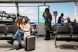 © DC Studio - Smiling woman uses a smartphone in an international airport hub while daydreaming about vacation, showing an upbeat traveler excited for a holiday trip and checking her phone before departure.