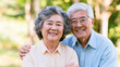 © Alexander - Smiling elderly Asian husband and wife posing outdoors with arms around each other, enjoying retirement together against a softly blurred natural background, senior couple, aging w