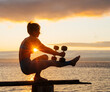 © Metadancer - White woman balancing with dumbbells on wooden beam at sunset by water
