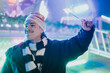 © qunica.com - Young man wearing a Santa hat and scarf smiles while holding a lit sparkler. A festive portrait of friends enjoying holiday lights at a nighttime fair.