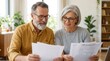 © Panuwat - Happy mature couple reviewing paperwork for retirement planning and financial advice.