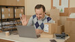 © Krakenimages.com - Man holding a cardboard box and gesturing toward a laptop while managing shipments in a parcel office storage area inside a building; entrepreneurial focus.