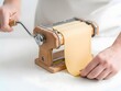 © MdSohel - Person making homemade fresh pasta dough using a classic manual metal and wooden pasta machine on a table