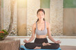© RooM The Agency - Young woman in sportswear sitting outdoors in a cross-legged lotus yoga pose (Padmasana) with her eyes closed and hands in a chin mudra pose practicing mindful meditation at an outdoor resort