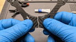 © MMCXIII - Close up of hands in blue nitrile gloves holding a broken carbon fiber drone frame prior to adhesive repair