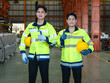 © Singh - Proud Asian Factory Technicians Giving Thumbs Up in Manufacturing Plant : engineer high-visibility safety jackets holding hardhat showing thumb-up gesture in modern industrial workshop.