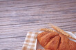 © Nurma - Golden croissants rest on a white plate. They sit atop a checkered napkin. Two wheat stalks lean beside the pastry. Wooden surface adds warm, rustic charm. Soft lighting highlights flaky
